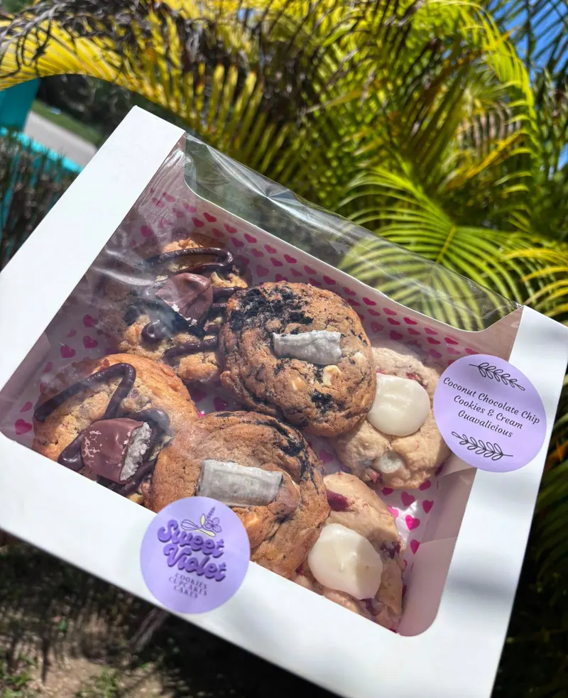 A window box of assorted cookies held up against palm fronds, with Sweet Violet stickers on the lid