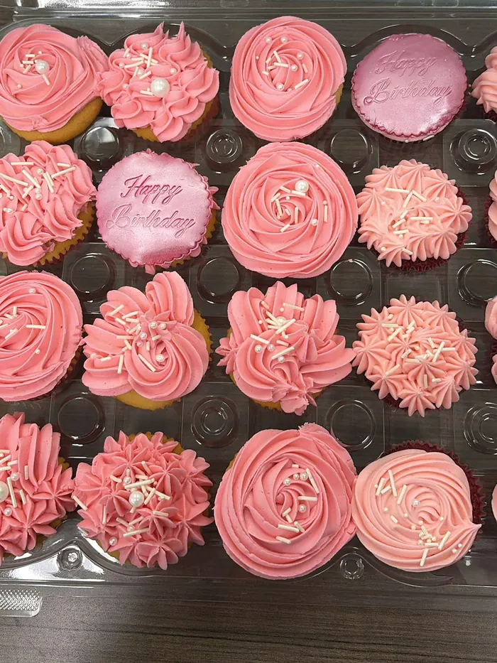 A tray of jumbo cupcakes piped with pink buttercream rosettes, pearls and Happy Birthday toppers